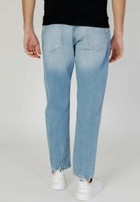 Jeans de mezclilla azul claro con corte relajado, diseño de cinco bolsillos, desvanecimiento sutil y costuras en contraste, combinados con zapatillas blancas.
