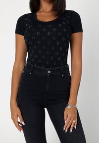 Czarna, dopasowana koszulka z krótkim rękawem, ozdobiona odblaskowymi okrągłymi wzorami, zestawiona z wysokim stanem czarnych dżinsów z detalami guzików.