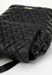 Schwarze Lederhandtasche mit einem gesteppten Herzmuster, featuring einer glatten Textur und einem kleinen Henkel. Goldene Hardware-Akzente auf der Vorderseite.