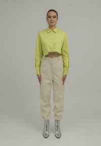 Limegrønn avkortet skjorte med knapper, kremfargede høytaljede bukser og sølvfargede ankelstøvletter med spiss tå. Minimalistisk design og tekstur.