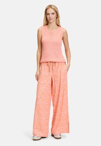  Lichtroze mouwloze gebreide top gecombineerd met wijde oranje gestreepte broek. De broek heeft een trekkoord en een bloemmotief. Zilveren schoenen.