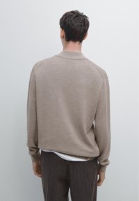 Maglione beige lavorato a maglia con maniche lunghe e colletto rotondo. Il tessuto sembra morbido con una trama sottile, sovrapposto a una camicia bianca.