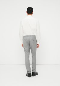 Camicia bianca a maniche lunghe, pantaloni grigi a righe sottili, scarpe nere. I pantaloni presentano tasche posteriori e un design slim fit.