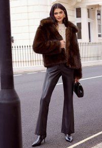 Ruda dirbtinės kailio striukė su gobtuvu, kreminės spalvos mezgimas, juodos odinės platėjančios kelnės ir blizgančios juodos stiletto basutės. Juoda rankinė.