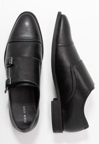 Chaussures en cuir noir avec une finition lisse, ornées d'une boucle, à bout rond et à petit talon. Détails de couture sur les côtés.
