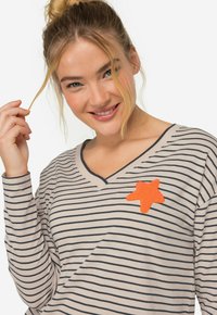 Randig långärmad skjorta i beige med marinblå ränder, med en orange stjärnformad applikation på bröstet. Mjuk tyg, V-ringad design.
