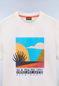Bela bombažna majica s pisanem grafičnim tiskom, ki prikazuje sonce, gore in kaktuse. Pod obliko je napis "NAPAPIJRI geographic".