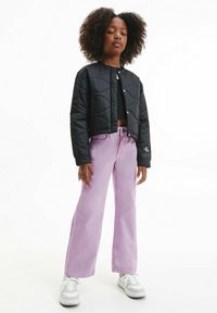 Giacca nera trapuntata con un design corto, abbinata a jeans larghi di un leggero colore viola. Il modello indossa sneakers bianche e un top corto nero.