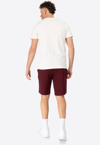 Hvid bomulds t-shirt med korte ærmer, parret med maroon shorts. Modellen har hvide strømper og sneakers på. Enkel design, ingen mønstre.