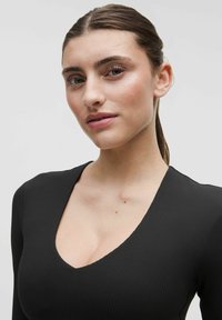 Top negru cu dungi, cu decolteu adânc în formă de V și mâneci lungi. Textură netedă, croială ajustată, evidențiind pielea de sub gât.