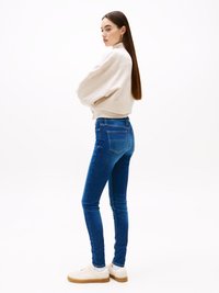Tynne blå jeans med en glatt denimtekstur, parret med en lys beige genser og hvite sneakers med brune såler.