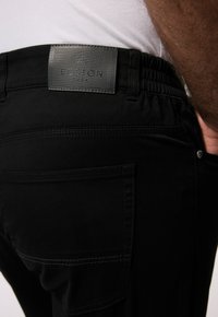 Pantaloni neri con elastico in vita, caratterizzati da una toppa in pelle con la scritta "BOSTON PARK" e una cucitura distintiva sulle tasche posteriori.