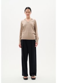 Maglione beige a collo a V lavorato a maglia con polsini e orlo a coste, abbinato a pantaloni neri larghi. Design semplice, texture leggera.
