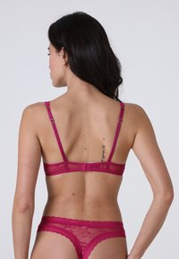 Reggiseno in pizzo magenta e perizoma coordinato con spalline regolabili, motivo floreale e chiusura con gancio e occhiello sul retro. Texture morbida, design semitrasparente.