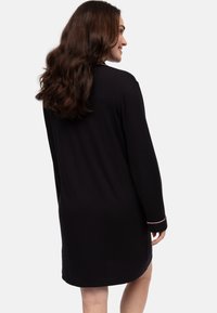 Vestido negro de manga larga, hecho de un material suave, con dobladillo redondeado y acentos en rosa contrastantes en los puños. Diseño minimalista.