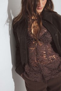 Brown suede jacket layered over a sheer brown lace top with floral patterns and button details. Minimalistic design with textured elements.