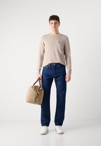 Suéter de punto beige, jeans rectos azul oscuro, zapatillas blancas y un bolso marrón claro con cremallera y asas marrones. Sin patrones notables.