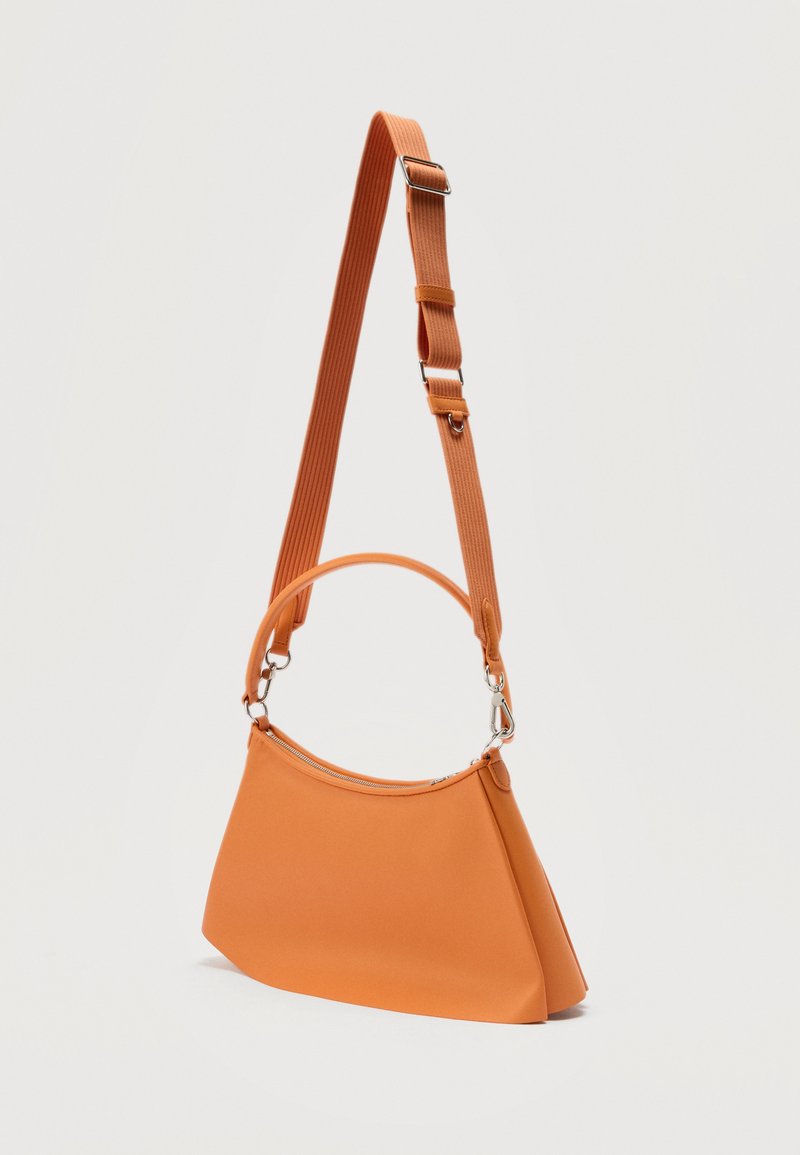 Orange trapezoid-shaped handbag with silver zipper, short handle, and adjustable long shoulder strap against a plain light background.