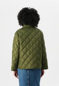 Veste matelassée vert olive avec un motif en losanges, dotée d'un col rabattu et de manches longues, associée à une jupe en denim bleue.