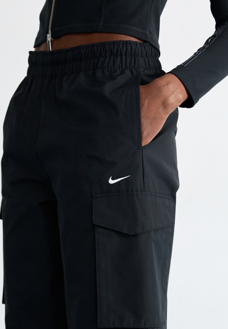 Schwarze Nike Cargo-Hosen mit elastischem Bund, seitlichen Taschen und einem kleinen weißen Logo am linken Bein, aus strukturiertem Stoff gefertigt.