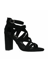 Zwarte suède hoge hak sandaal met meerdere kruislings gesneden banden, een gespsluiting en een chunky blokhak voor stabiliteit.