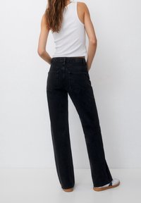 Jeans neri a vita alta con design a gamba dritta, dotati di tasche posteriori e dettagli di cucitura minimi, abbinati a un top bianco senza maniche.