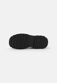 Suela de zapato negra con surcos horizontales pronunciados, hecha de goma; diseñada para ofrecer tracción con una punta redondeada y un acabado texturizado.