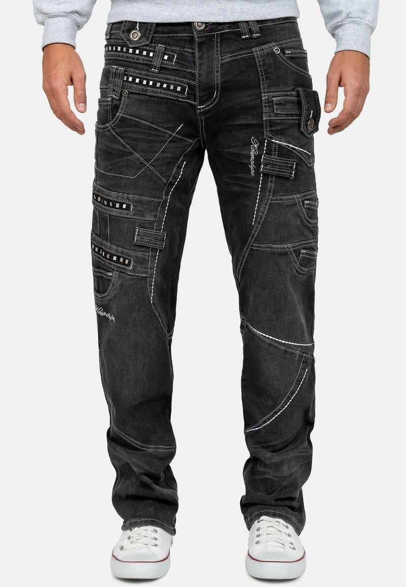 Pantaloni in denim neri con molteplici tasche, cuciture bianche a contrasto e dettagli distintivi come rivetti e accenti ricamati.