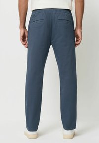 Hose mit elastischem Bund in Marineblau, mit glatter Textur, zwei Gesäßtaschen und geradem Schnitt, kombiniert mit weißen Sneakern.