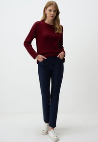 Pull en maron tricoté avec un col rond, assorti avec un pantalon slim fit bleu marine foncé et des baskets blanches. Texture lisse avec des manches longues.