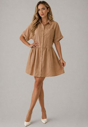 Femme portant une robe beige à manches courtes avec boutons, jupe froncée et talons blancs pointus, debout devant un fond uni.