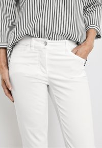 Pantalones de algodón blancos con corte ajustado, que cuentan con bolsillos frontales y un detalle de botón plateado en la cinturilla. Combinados con una blusa a rayas en blanco y negro.