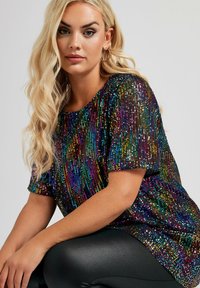 Top de manga corta cubierto de lentejuelas multicolores con un ajuste holgado, que presenta un escote redondeado y una base de leggings negros lisos.