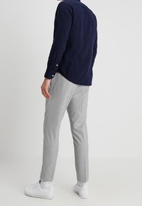 Námořnická košile s dlouhým rukávem, šedé zúžené kalhoty a bílé tenisky. Jednoduchý design, detaily na knoflících, měkké textury a neutrální barvy.