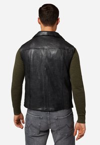 Schwarze Lederweste mit glatter Oberfläche, ausgestattet mit einem Reverskragen und sichtbaren Nähten, getragen über einem grünen Langarmhemd.