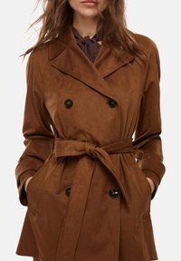 Cappotto doppiopetto in suede marrone con cintura in vita, bottoni neri e tasche laterali, dotato di colletto a rever e maniche lunghe.