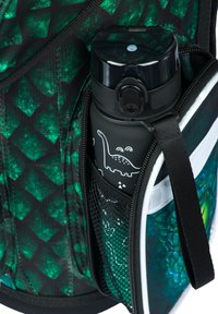 Czarna butelka na wodę z grafiką dinozaura, umieszczona w siatkowej kieszeni plecaka o zielonym wzorze, z białym, jednolitym wykończeniem.