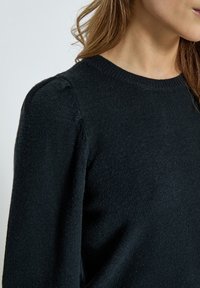 Black knit sweater with a round neckline and slight puff sleeves, featuring a soft texture and a fitted body silhouette.