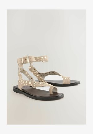 Sandale bej din suede cu un design decupat și accente circulare aurii; talpă plată, brățară la gleznă cu cataramă, stil cu vârful deschis.