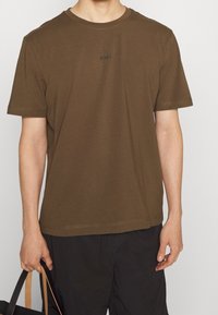 Brun t-shirt med rund hals i mjukt bomullsmaterial, med korta ärmar och en diskret "BOSS"-logotyp i mörkt broderi på bröstet.