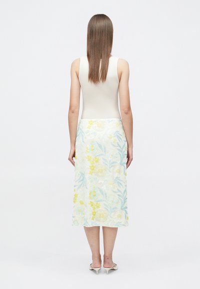Jupe midi fleurie avec broderie jaune et bleue sur fond clair, associée à un débardeur crème ajusté et des escarpins à bouts pointus.
