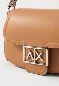 Tasche aus braunem Leder mit einem silberfarbenen Metallverschluss mit "AX"-Logo, glatter Textur, runder Form und gesteppten Akzenten am Klappenbereich.