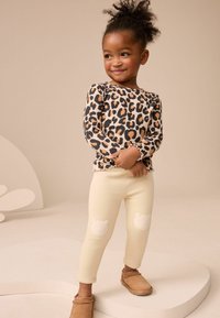 Top a maniche lunghe con stampa leopardata e orli arricciati, abbinato a leggings crema con toppe a forma di orso sui ginocchi e scarpe brown slip-on.