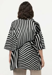 Överdimensionerad svartvit randig kofta med korta ärmar, med en texturerad tyg och en virvlande mönsterdesign.