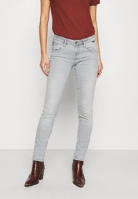 Ljust grå skinny jeans i denim, med framlommor och dragkedja. Kombineras med en röd skjorta och bruna texturerade klackstövlar.