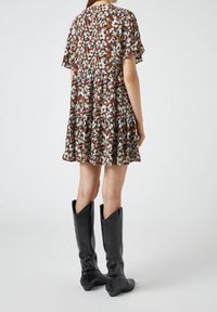 Blommig klänning i brunt, krämfärgat och blått, med korta fladdrande ärmar och en tjejad volangkjol. Matchad med slanka svarta knähöga stövlar.