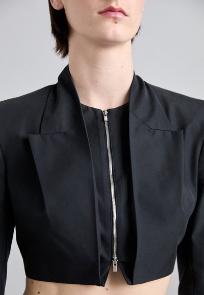 Black cropped jacket with a structured design, featuring a high collar, central zip closure, and pleated accents on the front.