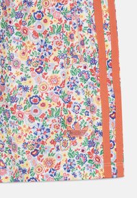 Tkanina s květinovým vzorem v několika barvách, obsahující červené, modré a žluté květiny. Zahrnuje oranžové boční pruhy a malé logo.