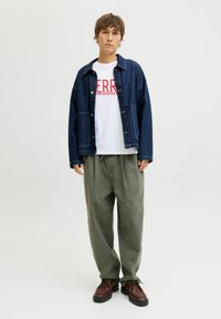 Donkerblauwe spijkerjack, witte t-shirt met rode tekst, losse olijfgroene broek en bruine leren schoenen met dikke zolen.