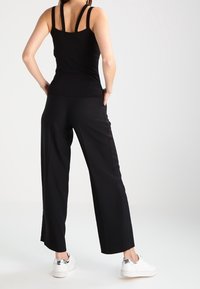 Czarny top bez rękawów z wąskimi ramiączkami, zestawiony z szerokimi czarnymi spodniami. Obuwie jest białe z srebrnymi akcentami. Gładki, dopasowany materiał.